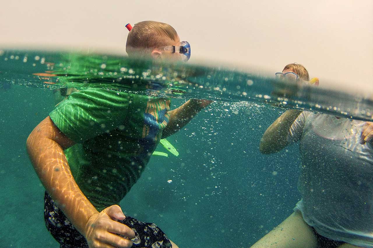 Zwei Personen beim Schnorcheln, halb unter Wasser fotografiert, während sie Spaß im klaren blauen Wasser haben.