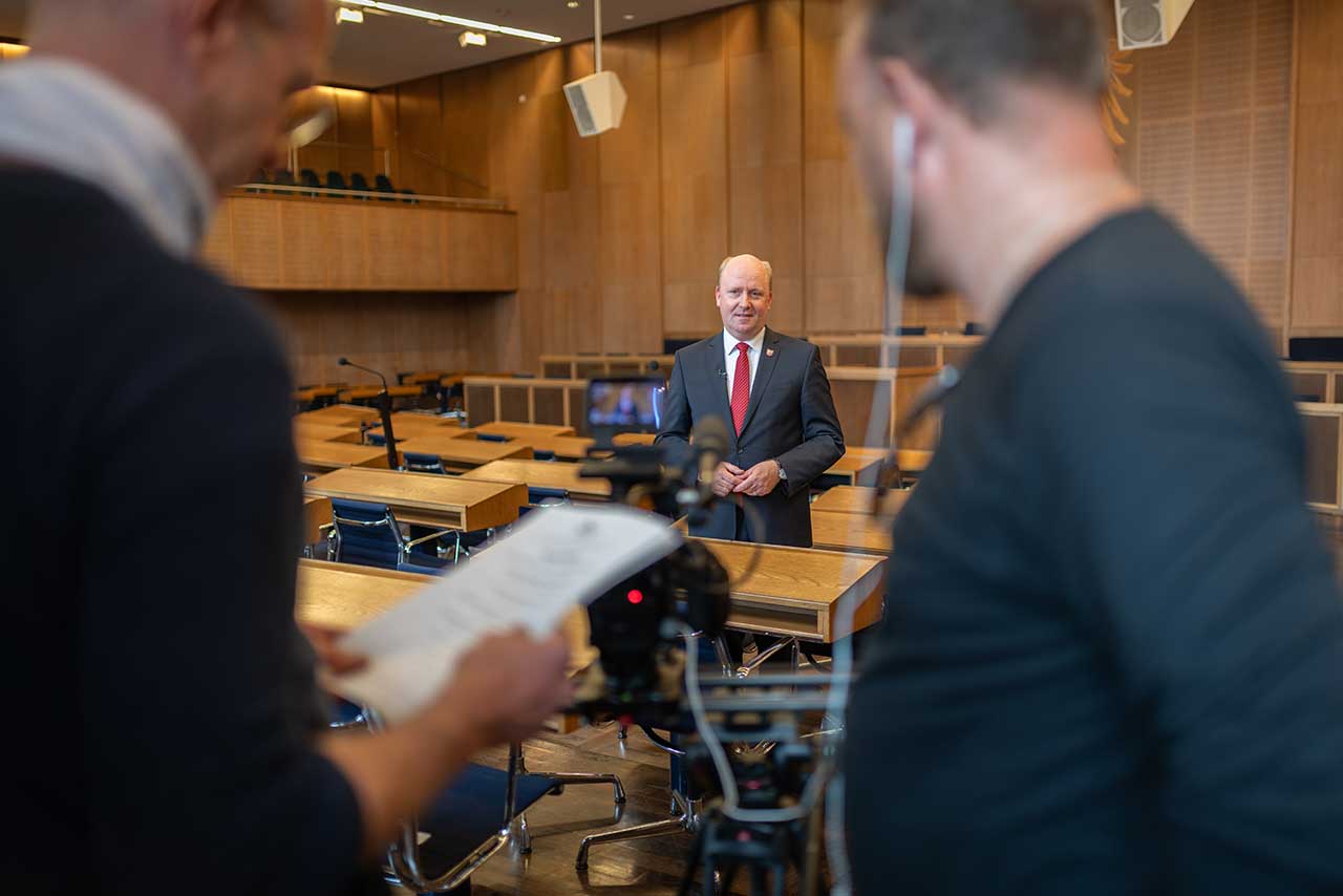 Zwei Männer beim Videodreh in Konferenzraum, im Fokus ein Sprecher vor der Kamera