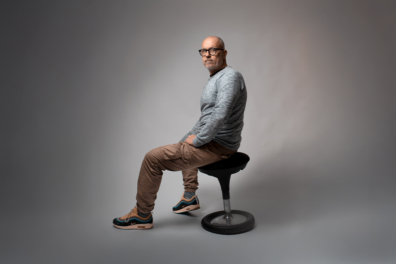 Porträt eines Mannes auf einem Hocker im Studio, seitlich sitzend, mit nachdenklichem Blick – symbolisch für innere Balance und Zurückhaltung.